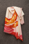 Lightweight merino wool stole with bold abstract floral print in red, orange, and pink tones, draped softly against a textured dark gray background – artisan-made in Nepal