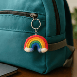 A close-up photo of a turquoise handbag adorned with a felted wool rainbow keychain, highlighting the playful charm and soft texture of the accessory.