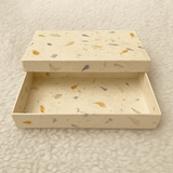 A handcrafted rectangular keepsake box made from natural Lokta paper embedded with dried flower petals and leaves, displayed open on a white surface.