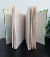 An inner view of a handmade A5 Lokta notebook with a solid green cover, standing upright on a dark wooden surface.